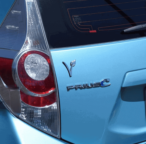 a silver vegan "v" emblem on the back of a light blue toyota prius
