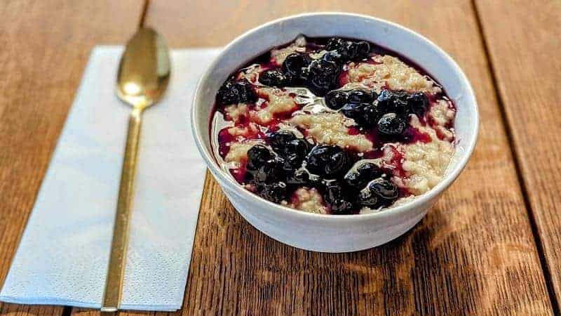 a large white bowl of vegan oatmeal topped with blue berry compote on a wood table in copenhagen