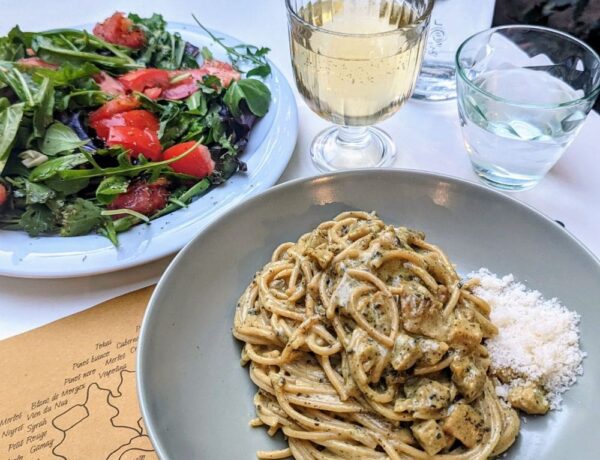 a bowl of creamy vegan pasta next to a green salad and a glass of wine at the vegan and vegetarian restaurant veg nirvana in florence