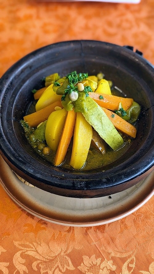 a black bowl filled with vegan vegetable tajine on a table covered with an orange tablecloth in morocco