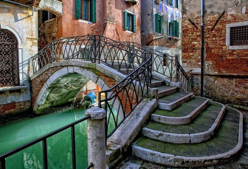 stone bridge with an iron railing over a green colored canal in venice italy
