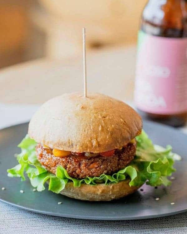 a vegan burger on a dark plate by itself with a bottle of soda in the background at the vegan restaurant vgoloso venice