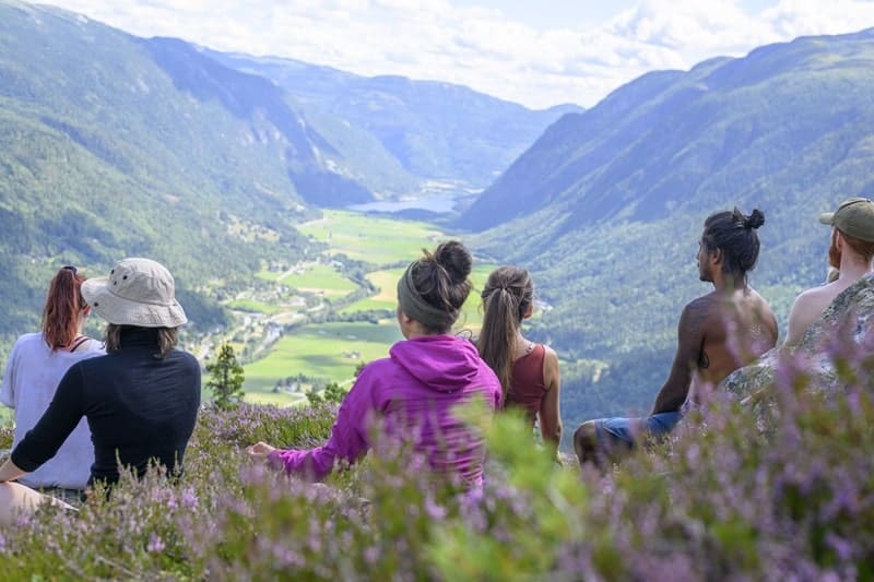 a group of yoga participants sitting on a hill that overlooks a norwegian valley surronded by beautful mountains in the summer at wanderlust yoga