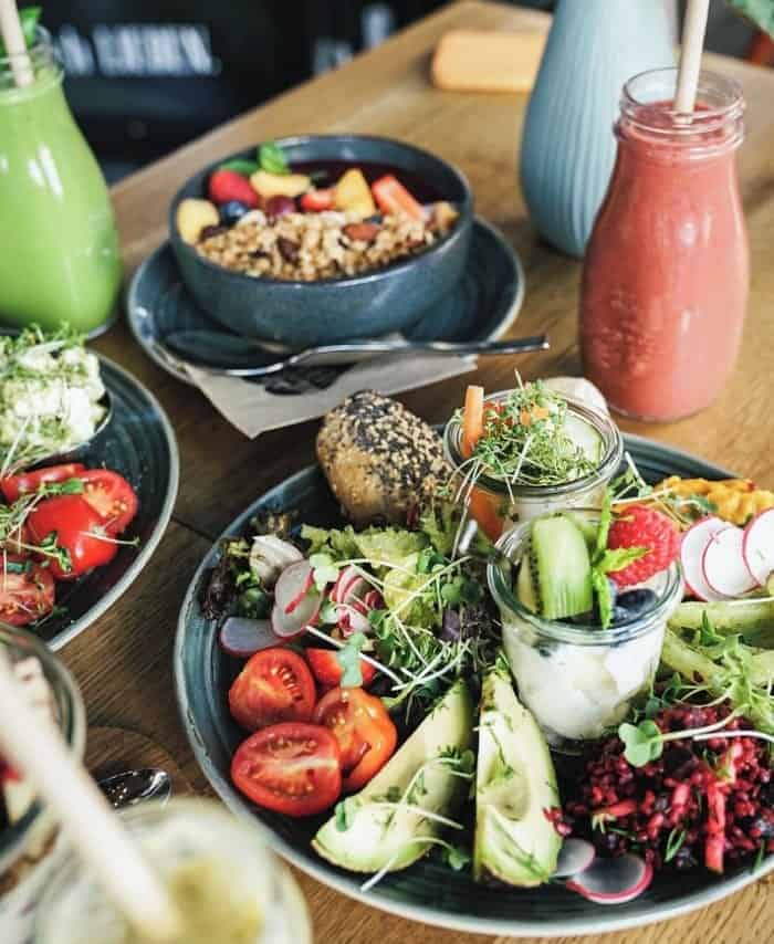 a large breakfast plate filled with toast and veggies next to a granola bowl and green and pink smoothie at was-wir-wirklich-LIEBEN.-Deli in  hamburg