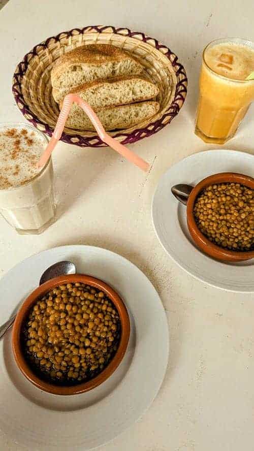 two bowls of vegan lentil stew with a basic of bread and two smoothies on a white table at the world storytelling vegan cafe in morocco