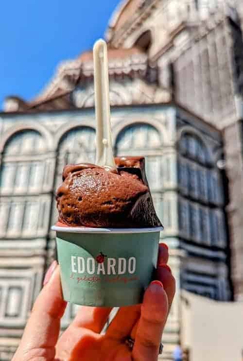a scoop of dark chocolate vegan gelato in a green cup held in front of the duomo in florence