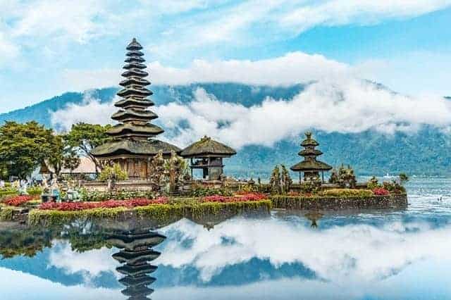 a balinese temple at the end of a peninsula surrounded by water with a fog covered mountain in the background