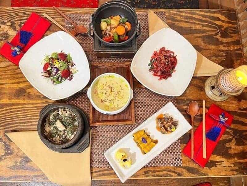 spread of vegan korean dishes on a wood table next to red napkins and chopsticks at hangawi in nyc