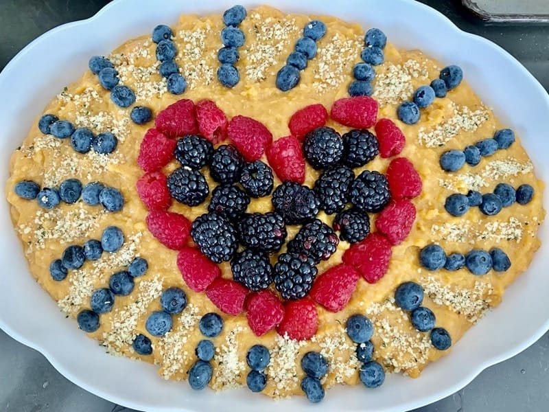 vegan mango smoothie bowl topped with blueberries and raspberries in the shape of a heart