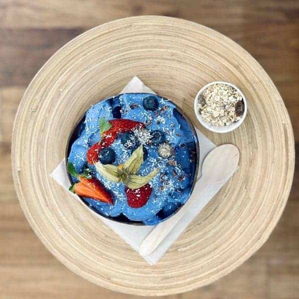 blue vegan smoothie bowl topped with fresh fruit on a wood table from raw firenze in florence
