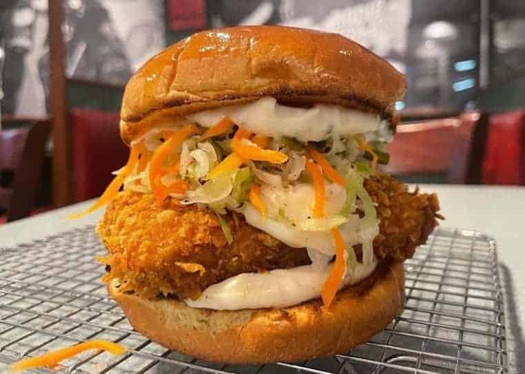 a massive vegan fried chicken sandwich with coleslaw and mayo sitting on a wire rack at superiority burger in nyc
