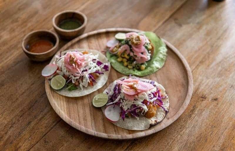 three vegan tacos on a wooden tray next to two bowl of sauces at the herb kitchen in bali