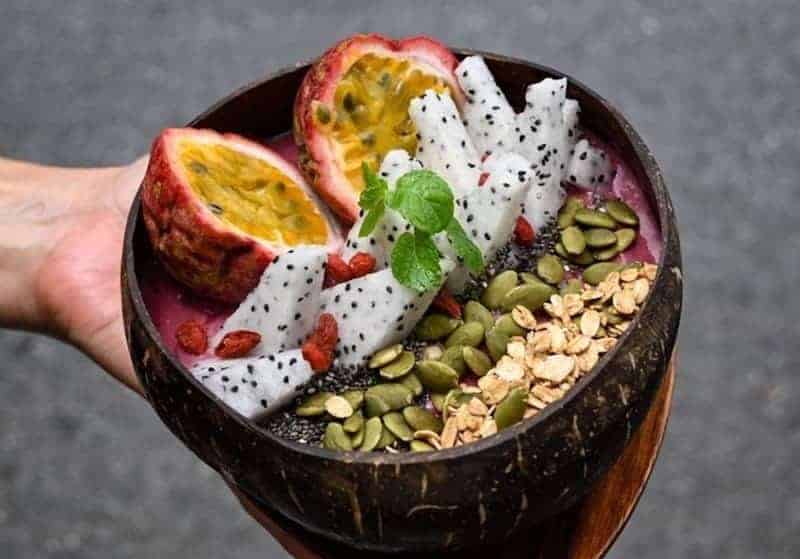 a small round smoothie bowl topped with halves of passion fruit, pitaya, and seeds