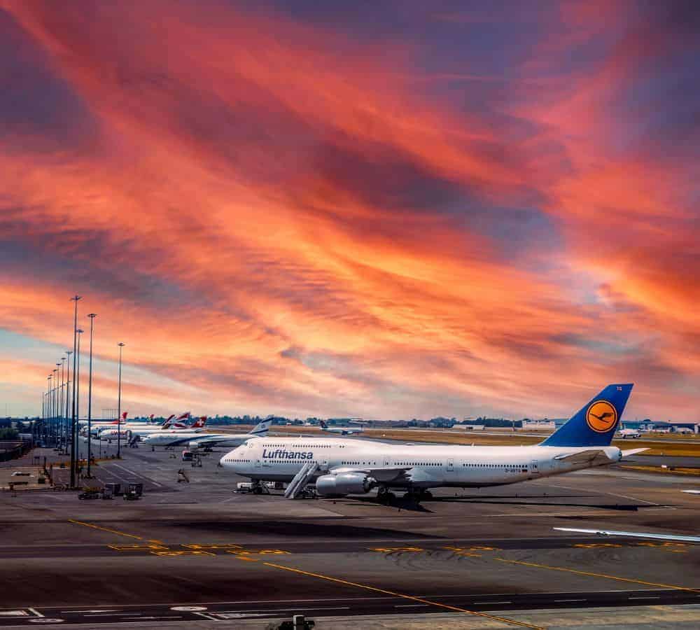 a single Lufthansa airplane parked at an airport with a beautiful pink and purple sky in the background