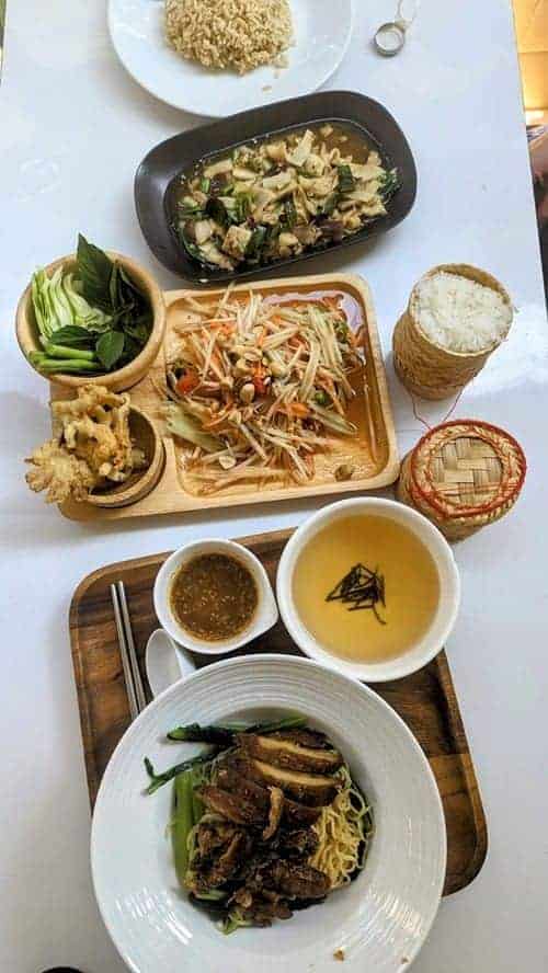 a spread of multiple vegan thai dishes on a white table at pai blu house in bangkok