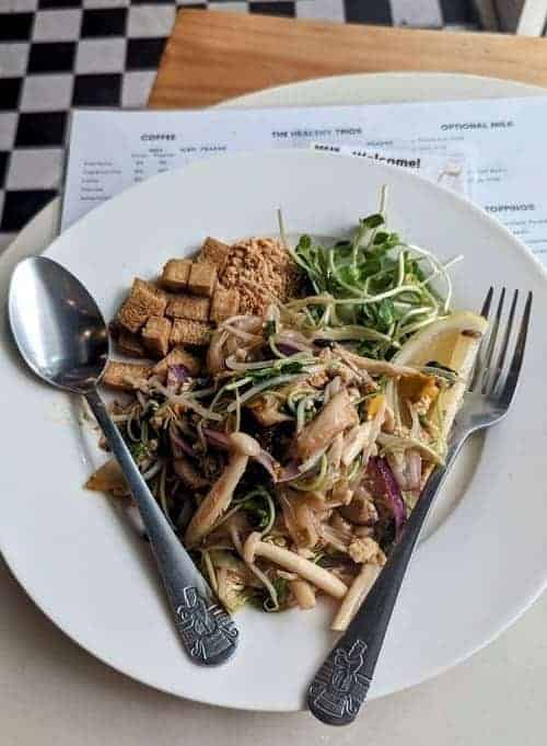a bowl of vegan pad thai with crispy tofu with a spoon and fork on either side at began vegan in bangkok