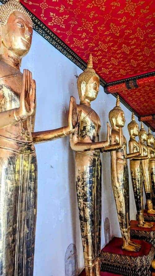 tall golden buddha statues standing in a line with their hands out flat signifying to stop fighting