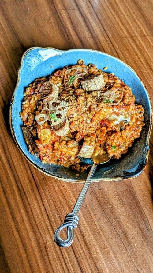 vegan tomato paella with mushrooms in a blue baking dish on a wood table at lazy farmers