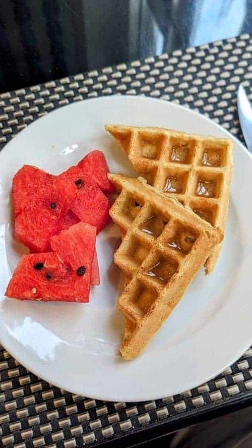 two vegan waffles on a plate next to watermelon