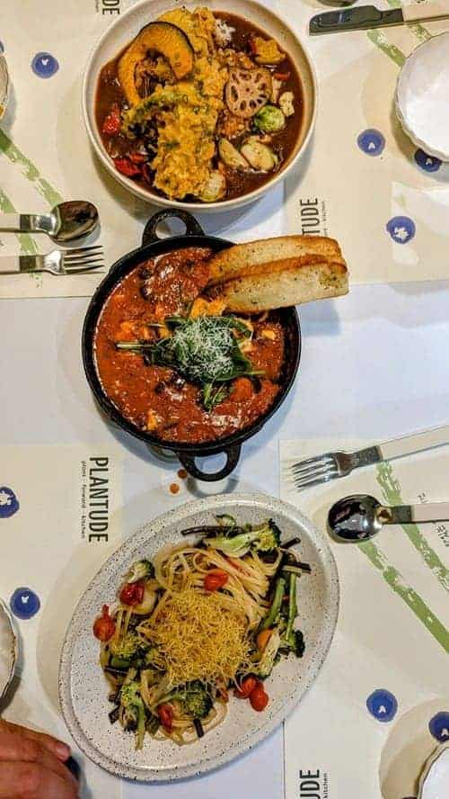 vegan pasta next to a tomato dish with a chunk of bread on a white table at plantude in seoul