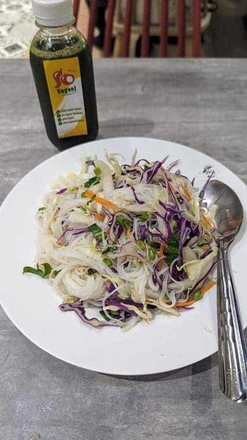 vegan and gluten free noodle salad with purple cabbage next to a green bottle of juice on a gray table