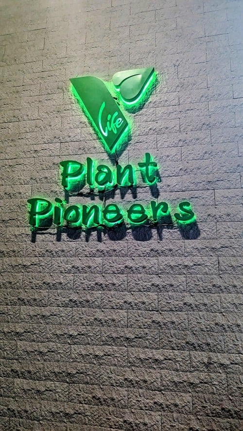 a green neon sign on a gray wall that says plant pioneers