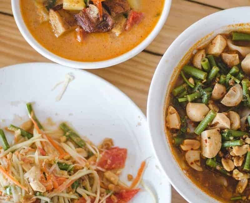 three vegan thai dishes on a light wood table 