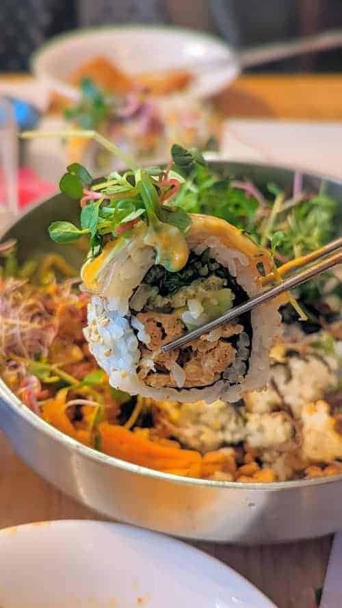 a single california roll held over a platter of food at vegan insa in seoul