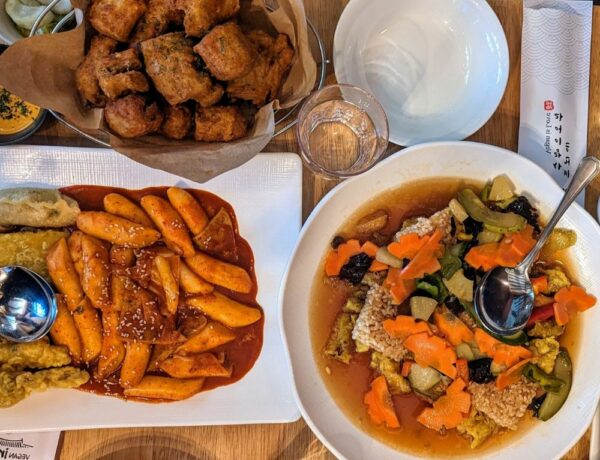 a large platter of sweet and sour veggies with rice next to korean rice noodles in tomato sauce and fried vegan chicken at vegan insa in seoul