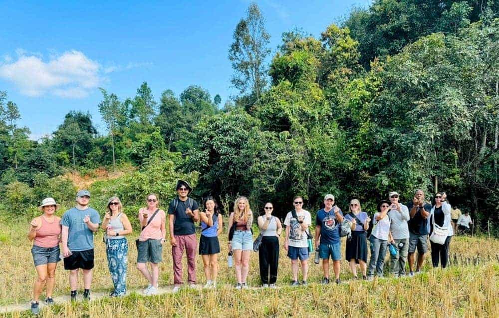 a group of people standing in a green field in thailand on a sunny day