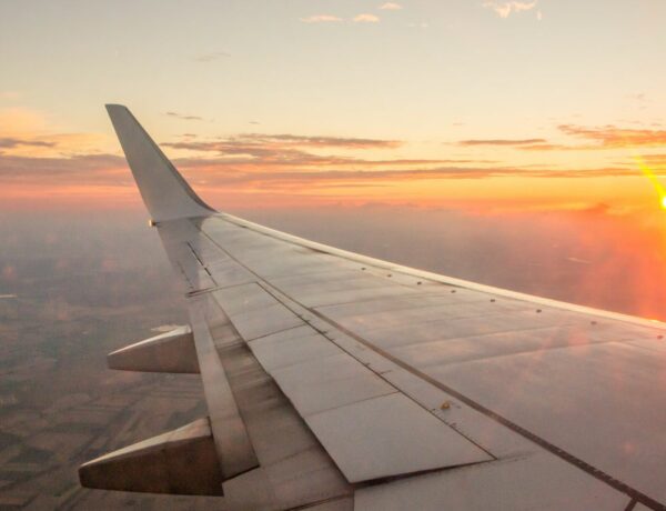 an airplane wing as it cuts through a partially cloudy orange sunrise in the sky