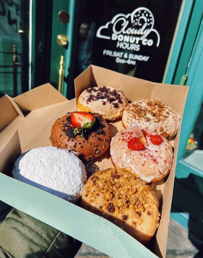 a box of six colorful vegan donuts topped with chocolate, powdered sugar, berries and more from cloudy donut co in brooklyn
