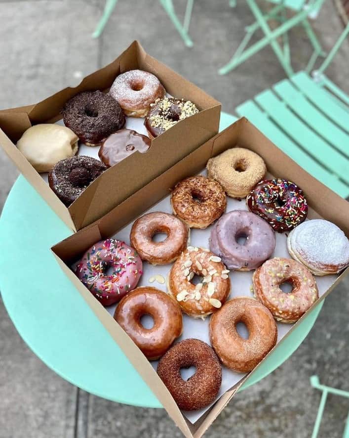 two boxes of round vegan cake donuts topped with glaze, powdered sugar, coconut and more from dun well doughnuts in brooklyn