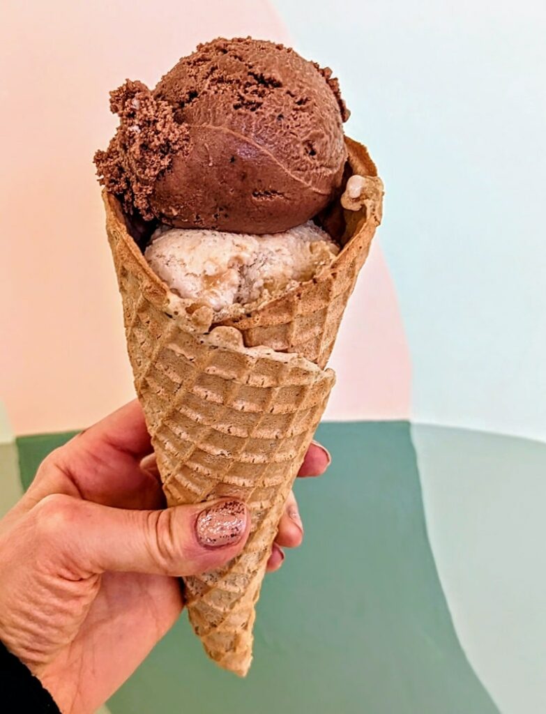 a large vegan waffle cone filled with two scoops of vegan ice cream held in front of a pink and green wall in portland