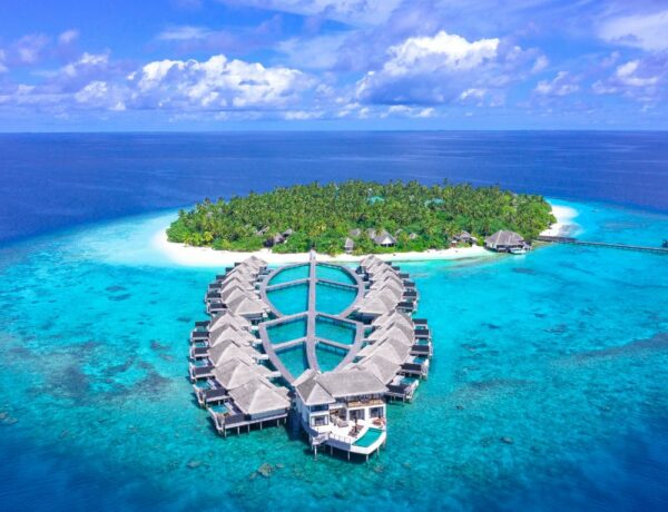 two strips of overwater bungalows connected to a small island in the maldives and surrounded by an endless ocean of blue waters