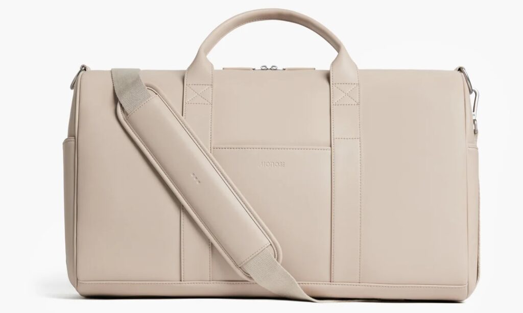 ivory vegan leather weekender bag with the strap across the front on a white background from monos