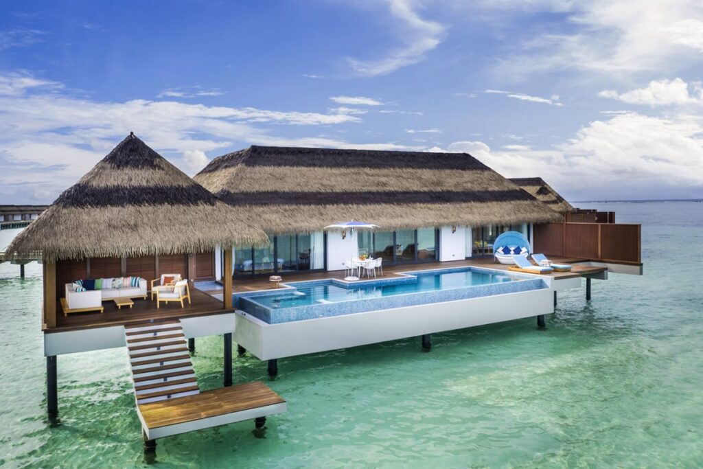 a thatched roof overwater bungalow in the middle of the blue ocean in the maldives at the pullman resort 
