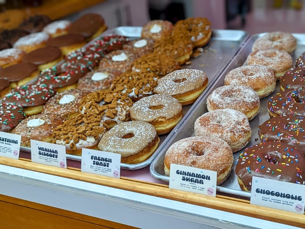 a dessert case filled with rows of vegan donuts covered in chocolate, nuts, and sugar and stuffed with cream