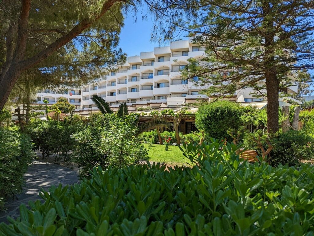 outside of the large, white, vegan-friendly resort apollonia which is surrounded by lush greenery on a bright and sunny day on crete