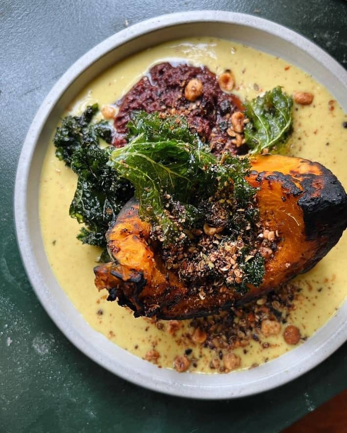 a large piece of golden roasted squash in a pool of yellow cream sauce with kale at the vegan restaurant bubula in london 