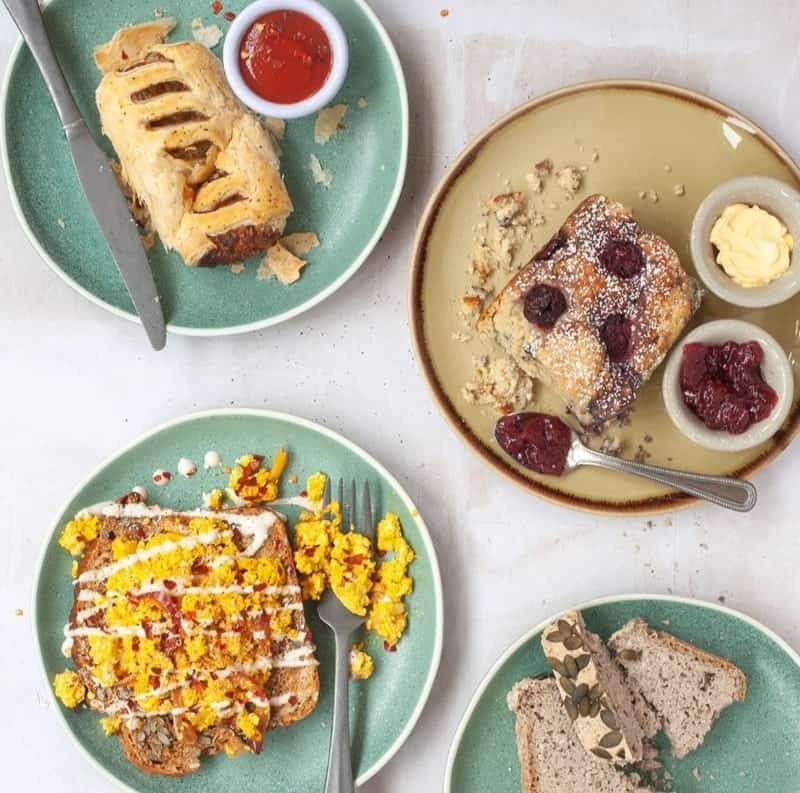 a vegan breakfast spread with a sausage roll, tofu scramble on toast, and a baked oatmeal on a white table at cornucopia in dublin, ireland