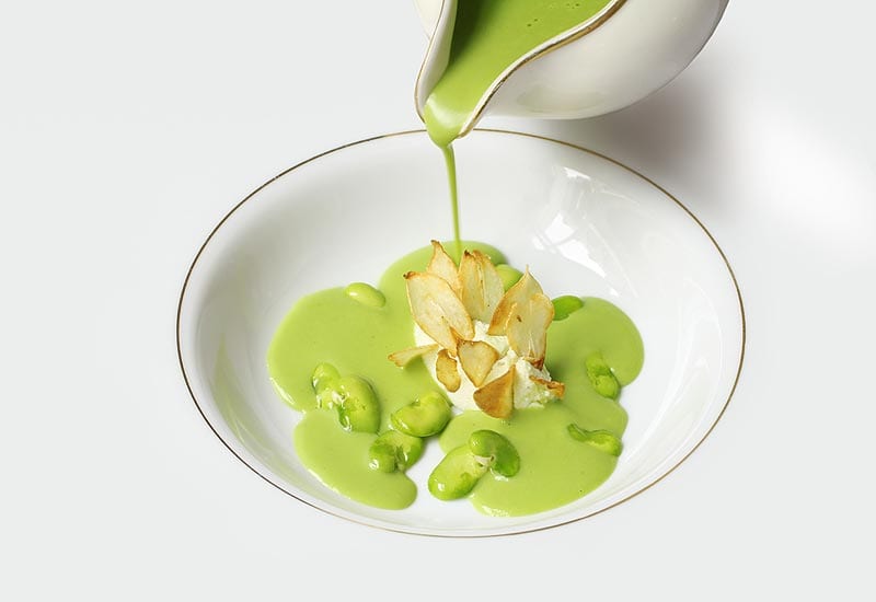 beautiful white bowl being filled with a green sauce from a gravy boat overhead at the michelin starred restaurant gauthier soho in london 