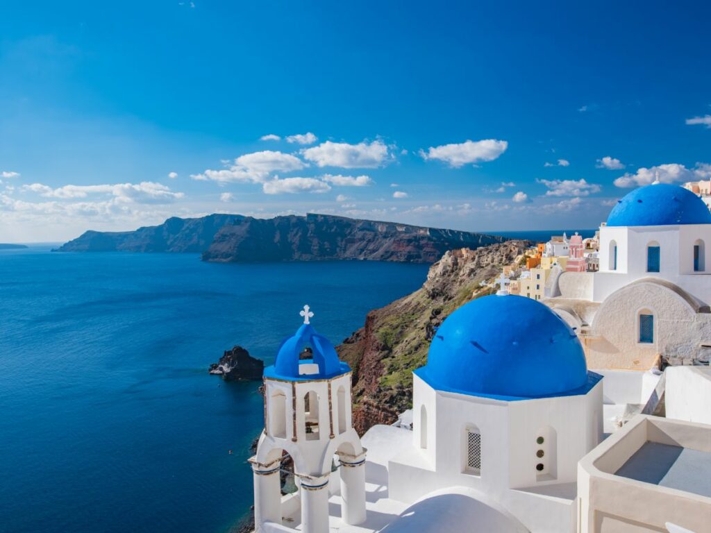 seaside cliffs in santorini, greece with the white washed buildings and blue domes poking out above the blue ocean