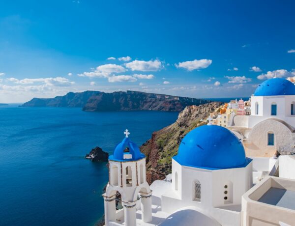 seaside cliffs in santorini, greece with the white washed buildings and blue domes poking out above the blue ocean