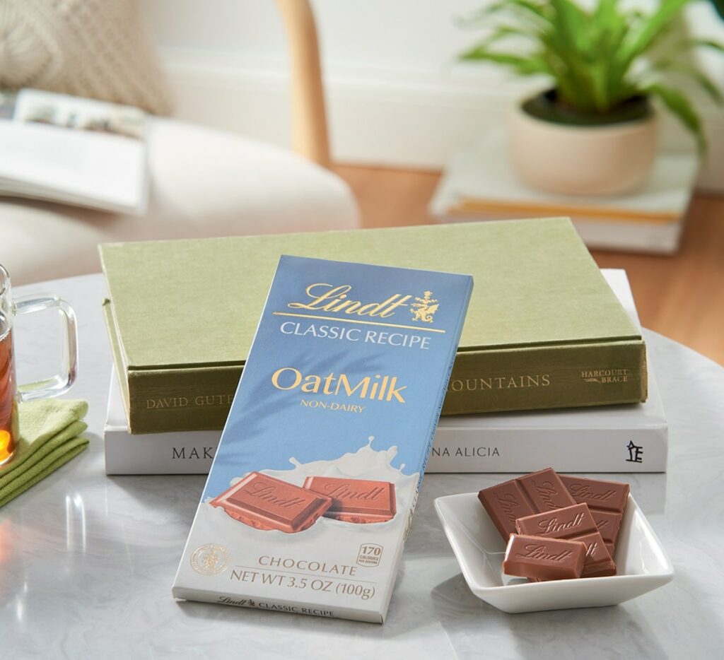 a bar of vegan oatmilk chocolate from lindt leaning again a green book next to a plate of vegan chocolate squares