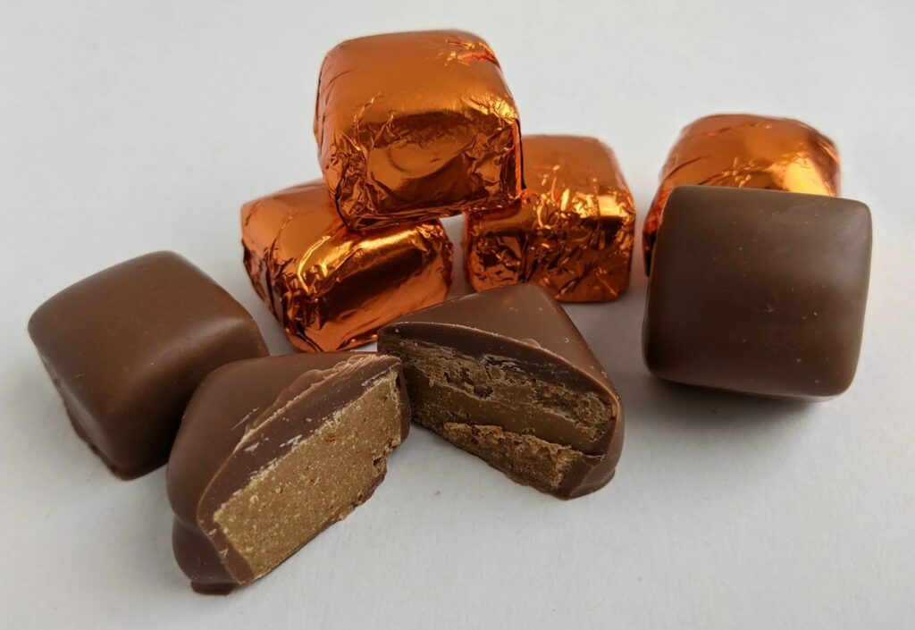 small squares of vegan milk chocolate peanut butter candies wrapped in orange foil 