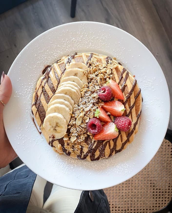 a white plate with a stack of pancakes covered in a chocolate and peanut butter drizzle and topped with slices of banana and strawberries at pog cafe in dublin