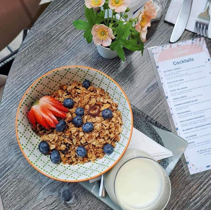 a small bowl of granola topped with strawberries and blueberries next to a glass of milk at almond butterfly bistro at brunch in toronto