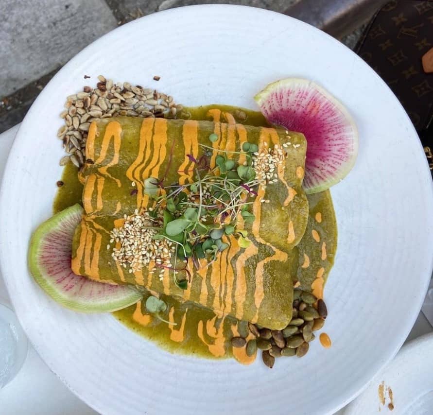 vegan enchiladas covered in a green mole sauce with a queso drizzle on a white plate at bar verde in nyc