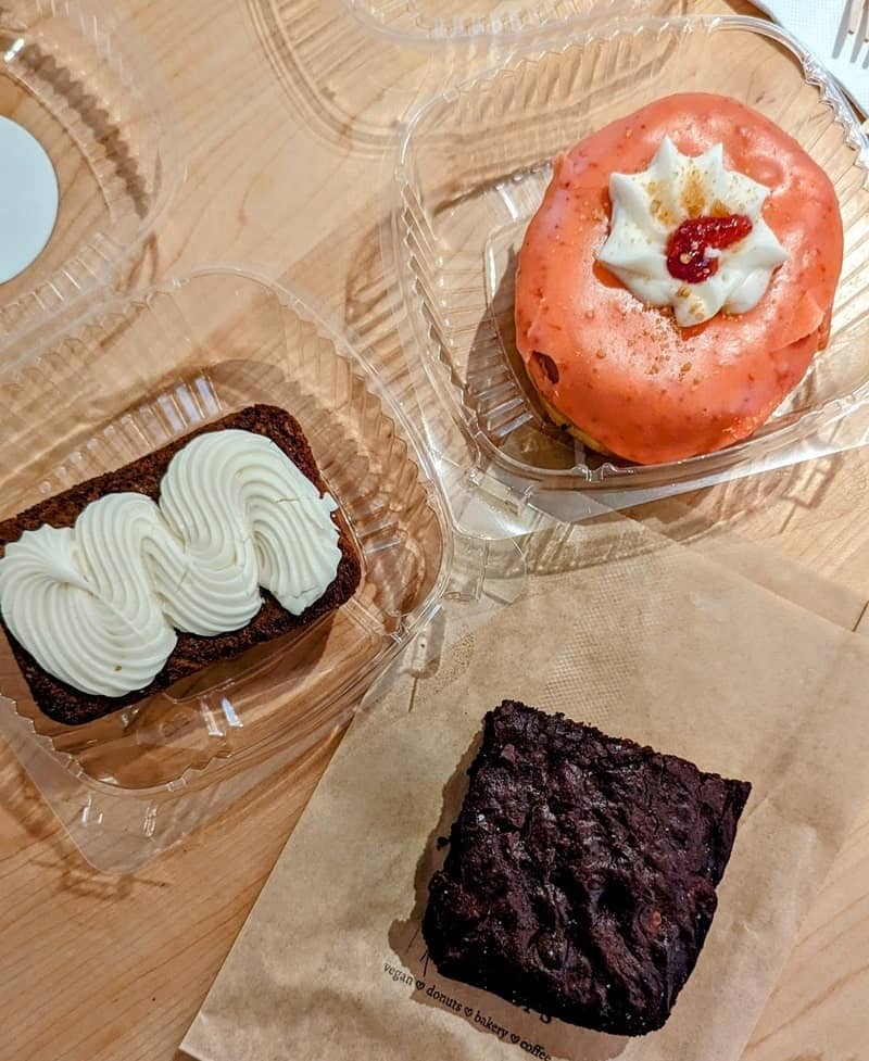 a pink vegan donut next to a large vegan brownie and a carrot loaf covered in frosting at bloomers in toronto